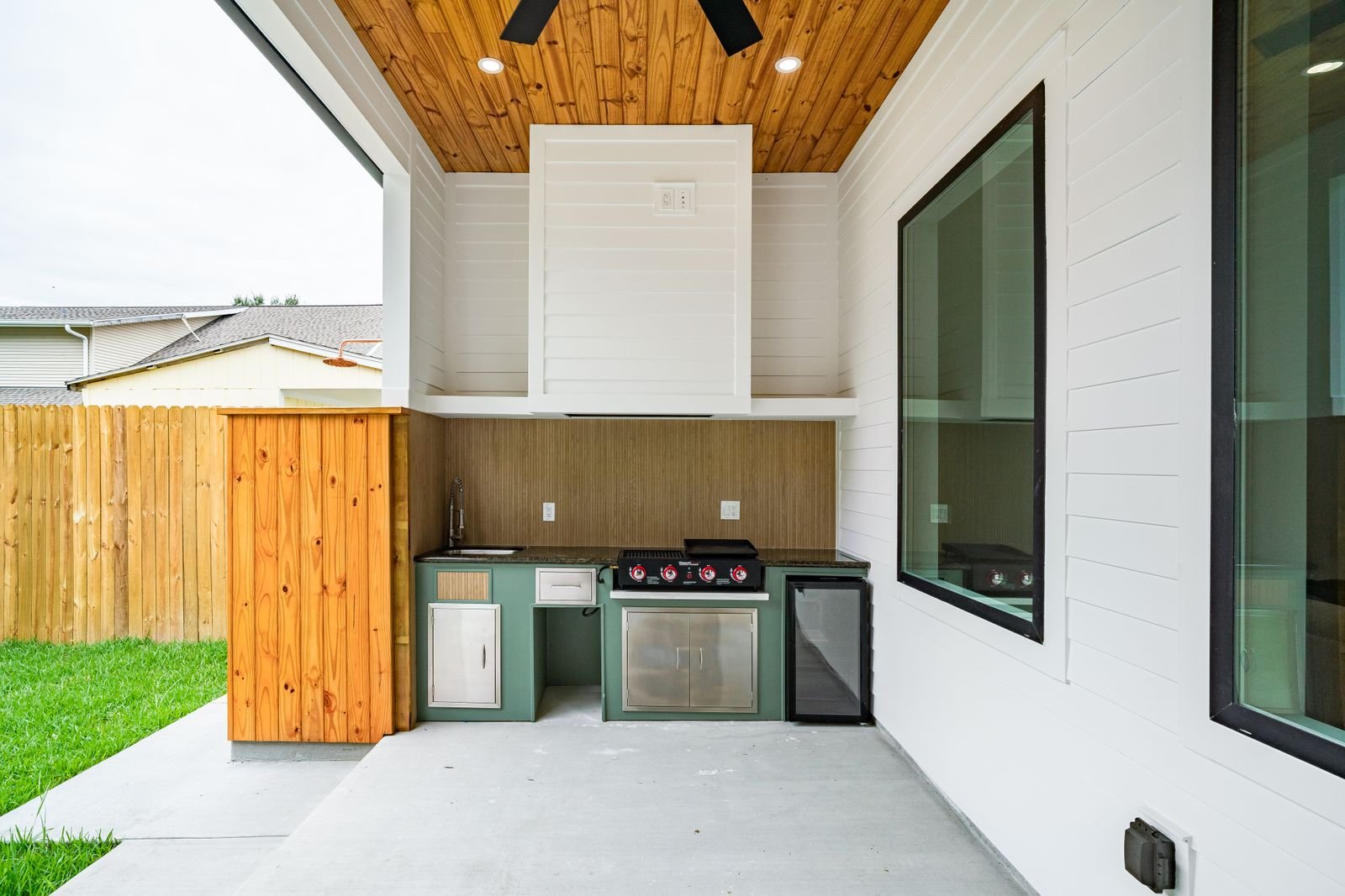 Built-in outdoor kitchen with a gas grill under a timber ceiling